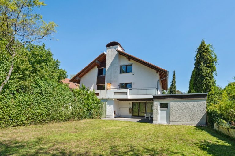Ein mehrstöckiges Wohnhaus mit einem großen Garten und einer Terrasse im Hintergrund.