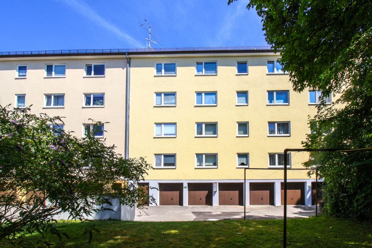 Gelbes Wohngebäude mit mehreren Fenstern und Garagen im Erdgeschoss.