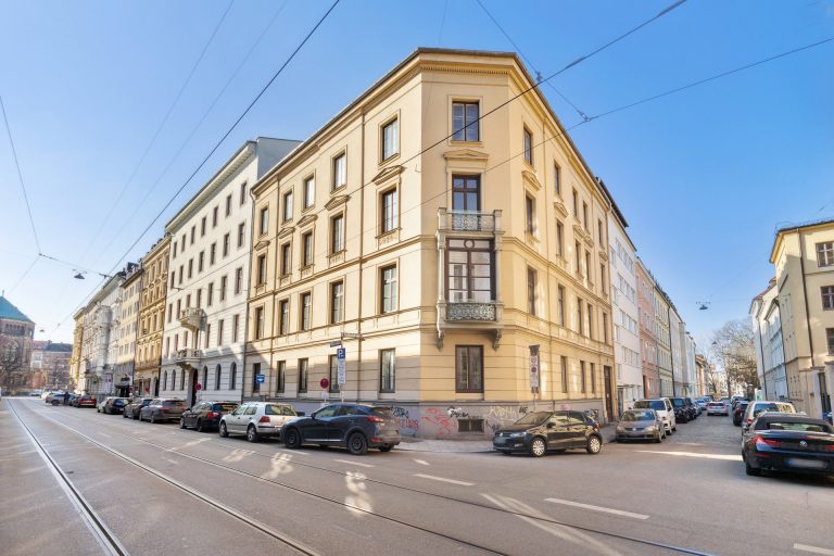 Eckgebäude mit klassischer Architektur in einer städtischen Umgebung, umgeben von parkenden Autos.