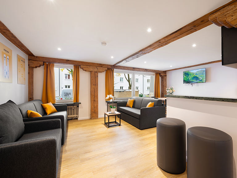 Modernes Wohnzimmer mit grauem Sofa, orangefarbenen Kissen und einem Fernseher an der Wand.