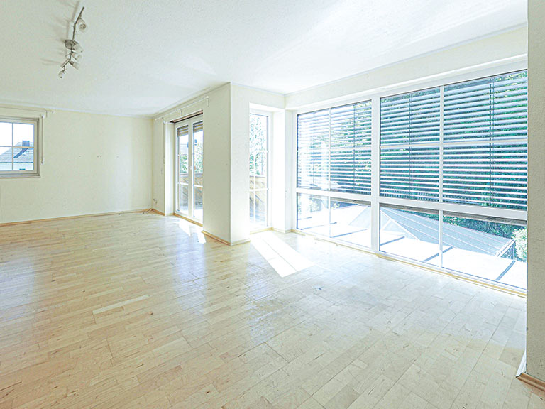 Heller Wohnraum mit Holzfußboden und großen Fenstern, die Tageslicht hereinlassen.