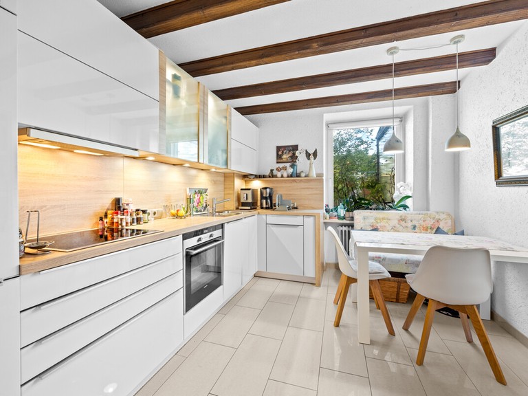 Helle moderne Küche mit weißen Schränken, einem Esstisch und Holzdetails im Design.