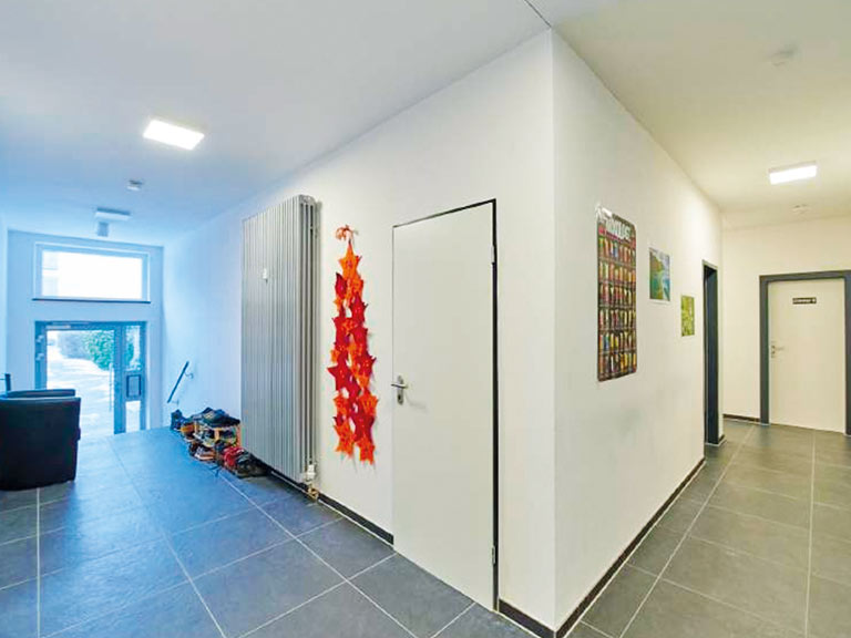 Flur mit grauen Fliesen, Heizkörper und Wanddekoration in einem modernen Gebäude.