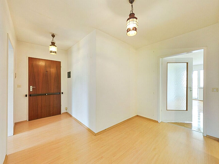 Helles Wohnzimmer einer 2-Zimmerwohnung in München, Objekt-ID R-7692: weiß verputzte Wände, Holzboden, Türen und moderne Deckenleuchten im Innenraum.