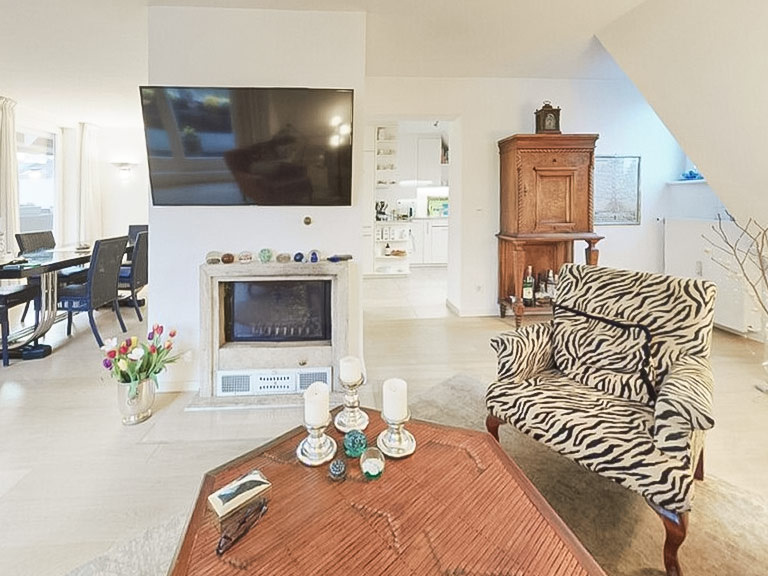 In einer hellen Wohnung in Lehel, München stehen ein Zebra-Sessel, Kamin, TV und antike Möbel in einem offenen Wohnbereich.