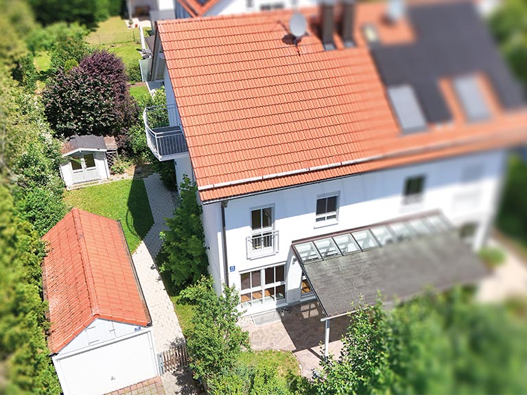 Weißes Doppelhaus mit roten Ziegeldächern, Garten, Garage und überdachtem Eingangsbereich in Grasbrunn bei München
