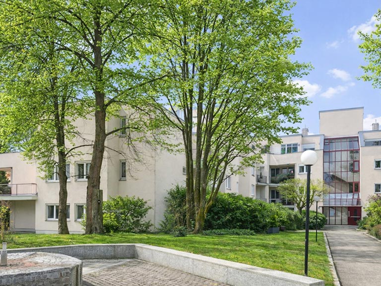 Gepflegte Wohnanlage mit grüner Außenfläche, hohen Bäumen und modernen Mehrfamilienhäusern in München
